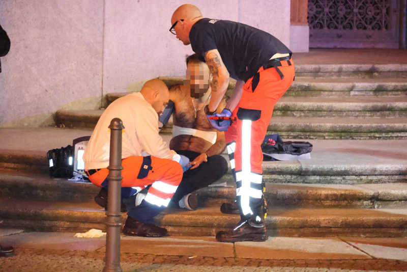 Einer der verletzten Männer mit Rettungssanitätern. Er trägt einen Druckverband.